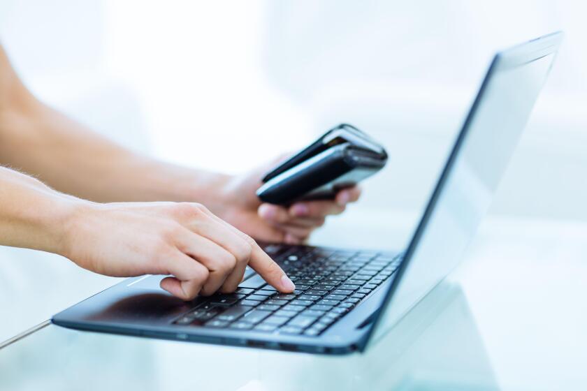 Online banking, shopping and booking. Closeup of a person's hand holding a wallet while using a laptop computer.