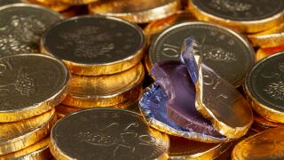 Chocolate money pile of gold coins. Edible sweets covered in foil as pretend money. One open coin half eaten