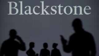 The Blackstone logo is seen on an LED screen in the background while a silhouetted person uses a smartphone in the foreground (Editorial use only)