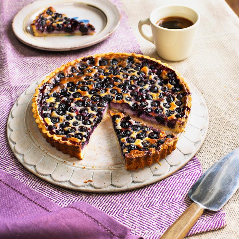 Blueberry cream cheese tart with slice cut away, cake server, coffee cup and separate slice on plate nearby