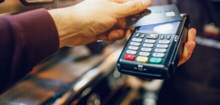 One hand hold machine for cards white another hold dark card for paying money. Men stand at coffee machine