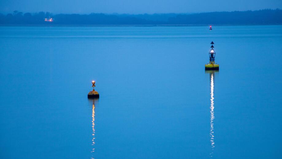 Two buoys marking the navigation channel.  Lights reflected on the water on a calm evening in winter.  The sea is pale blue.