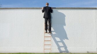 Businessman on ladder looking over wall