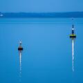 Two buoys marking the navigation channel.  Lights reflected on the water on a calm evening in winter.  The sea is pale blue.