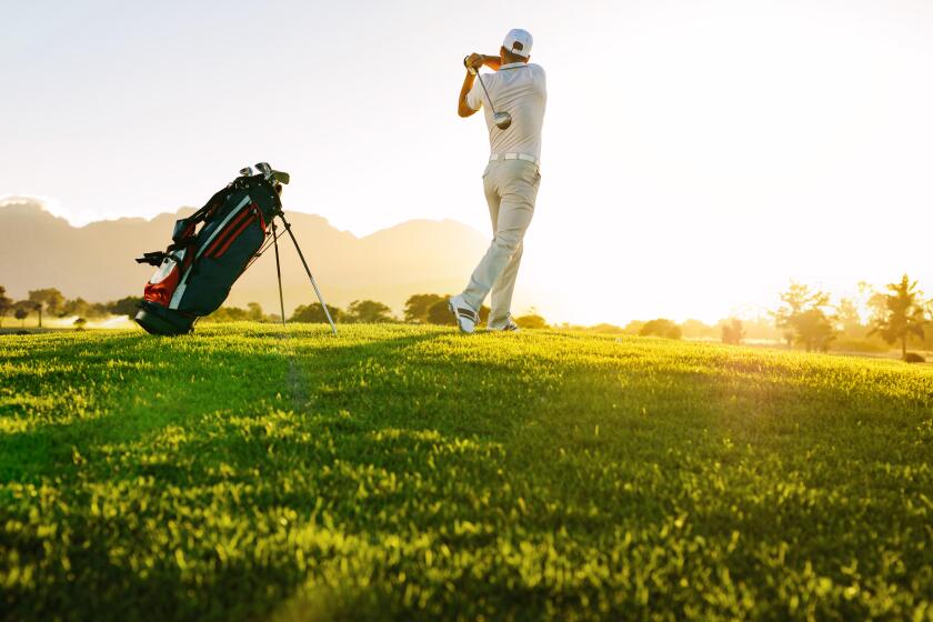 Low angle shot of professional golfer taking shot while standing on field. Full length of golf player swinging golf club on sunny day.