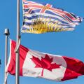 Canada and British Columbia flags waving over blue sky in Vancouver, BC, Canada
