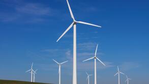 Wind turbines at windfarm in field against blue sky