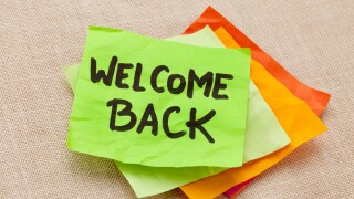 welcome back - handwriting on a green sticky note against canvas board