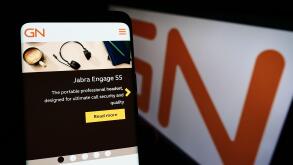 Person holding smartphone with website of Danish electronics company GN Store Nord AS on screen with logo. Focus on center of phone display.