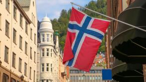 Typical street in Bergen, historic architecture, a Norweigan flag and  mountain of Floyen in the background on a summer day. Norway.