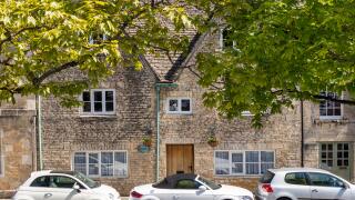 Old stone houses and new cars in the Market Place in the ancient Cotswold town of Northleach, Gloucestershire UK