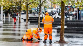 Two male employees of SGS in orange high-visibility clothing, making an inspection on the forecourt of King's Cross Station, London, UK