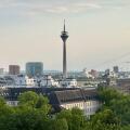 Dusseldorf skyline with Rheinturm tower, modern architecture, and the Rhine under a dramatic cloudy sky.