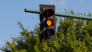 Traffic signal, orange light, amber light, or traffic light.  Blue sky and green trees in the background