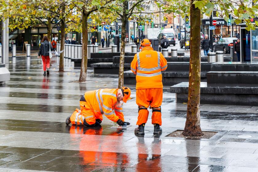 Two male employees of SGS in orange high-visibility clothing, making an inspection on the forecourt of King's Cross Station, London, UK