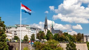 View over the Petrusse Valley Park to the Grand Hotel Cravat and Notre-Dame Cathedral. Luxembourg flag flies against a blue sky.
