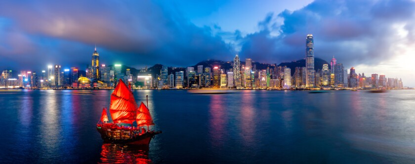 Panorama of Hong Kong City skyline with tourist sailboat at night. View from across Victoria Harbor HongKong.