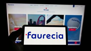 Person holding smartphone with logo of French automotive supplier Faurecia SE on screen in front of website. Focus on phone display.