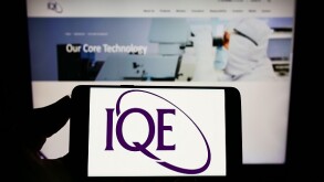 Person holding smartphone with logo of British semiconductor company IQE plc on screen in front of website. Focus on phone display.