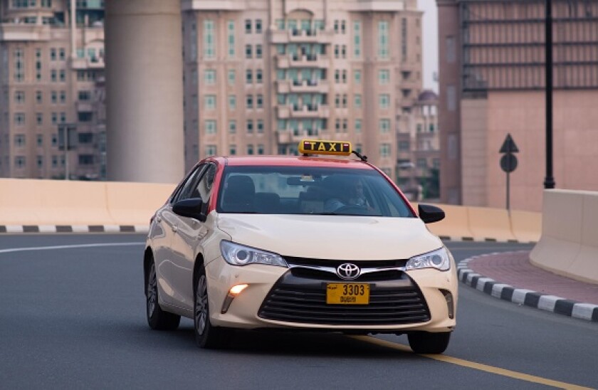 Close-up of Dubai Taxi as it passes a curve on the road in the urban city of Dubai, United Arab Emirates. Shot in the day. Buildings in the background.