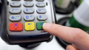 A finger pushing an approve button on a credit card machine.