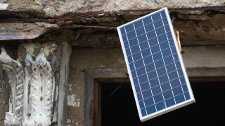 A solar panel hangs in the window of an old unmaintained building
