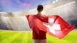 Switzerland football supporter on stadium. Swiss fan on soccer pitch watching team play. Young player with flag and national jersey