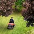 High angle view of a man using a ride-on mower to cut the grass in his back yard viewed between leafy green trees in spring or summer