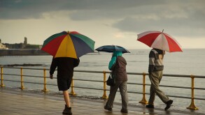 Three people sheltering under umbrellas on a wet summer evening, Aberystwyth Wales UK