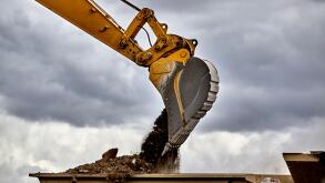 Construction industry heavy equipment excavator moving gravel at jobsite quarry with stormy skies