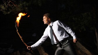 Image of brave man with burning stick in darkness