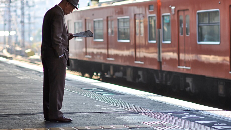 An elderly man reading a newspaper while waiting for a train.