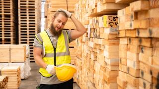 Portrait of a male worker with helmet and safety vest in wooden warehouse