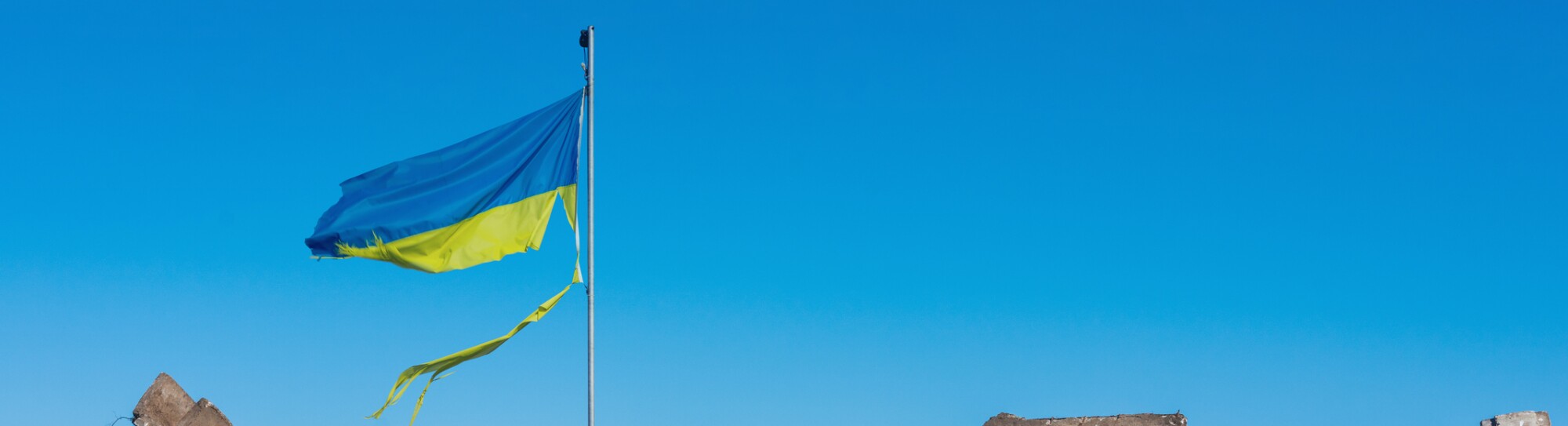 war in ukraine. Destroyed Ukrainian building and damaged flag in the wind.