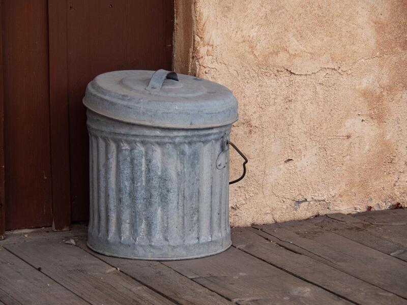 Galvanized metal ash can on a wooden walkway.