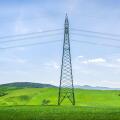 High voltage power line tower standing in a lush green field in Tuscany. Modern infrastructure in a rural spring landscape near Volterra, Italy