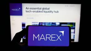 Person holding smartphone with logo of British financial services company Marex Group on screen in front of website. Focus on phone display.