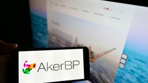 Person holding mobile phone with business logo of Norwegian oil and gas company Aker BP ASA on screen in front of web page. Focus on phone display.