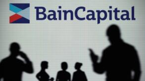The Bain Capital logo is seen on an LED screen in the background while a silhouetted person uses a smartphone (Editorial use only)