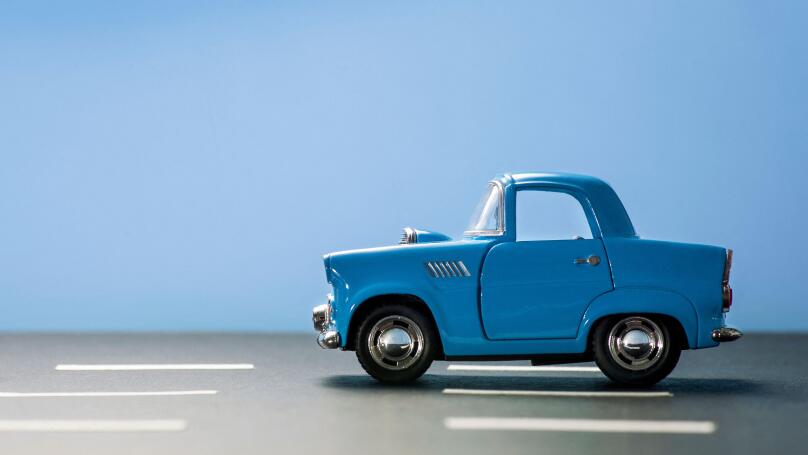 Side view of a blue toy car on a blue background and on an asphalt road.