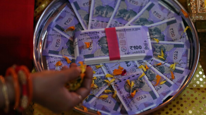 A woman puts flower petals on the new 100 Indian rupee notes as she prays as part of a ritual during Dhanteras, a Hindu festival associated with Lakshmi, the goddess of wealth, in Ahmedabad