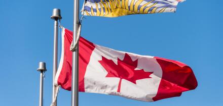 Canada and British Columbia flags waving over blue sky in Vancouver, BC, Canada