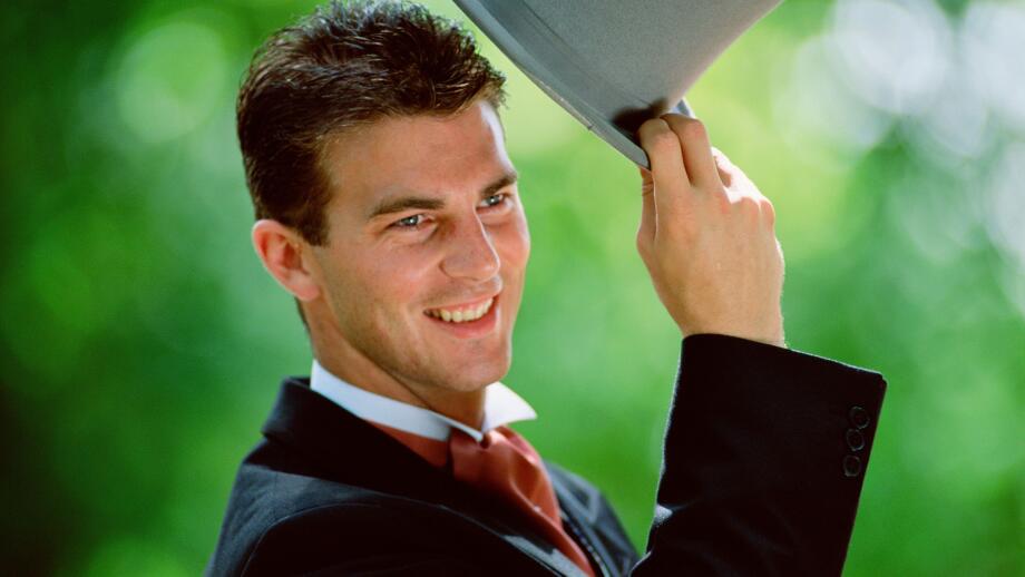 Lifestyle. Wedding. Man outdoors raising his top hat.