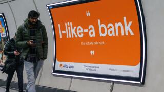 Commuters walk past an Advert for Allica Bank on wall of London railway station  London UK