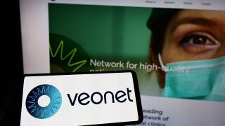 Person holding mobile phone with logo of ophthalmological clinic network Veonet GmbH on screen in front of web page. Focus on phone display.