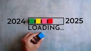 A hand is placing a blue block on a loading bar with colored blocks, representing the transition from 2024 to 2025. New year, new start concept.