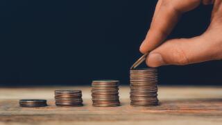 Coin stacks closeup with hand putting an US quarter on the top of the highest pile. Financial and business growth, economics, wealth, savings or banki