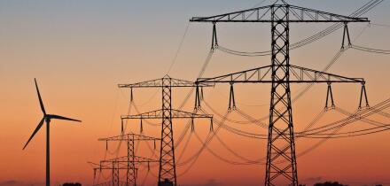 Silhouettes of a wind turbine and electric power posts during sunset