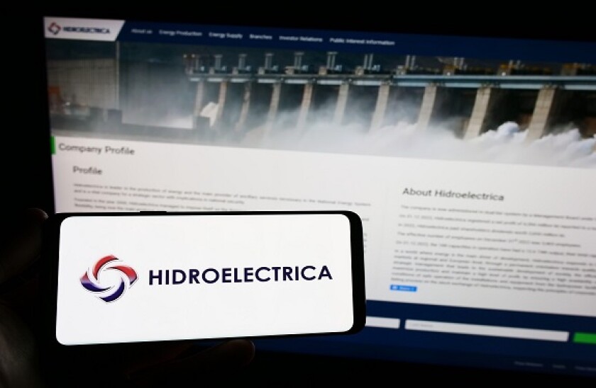 Person holding smartphone with logo of Romanian energy company Hidroelectrica S.A. on screen in front of website. Focus on phone display.