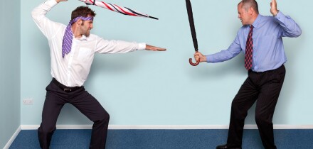 Photo of two businessmen having a sword fight using umbrellas, good image to convey conflict, rivalry or disagreement.